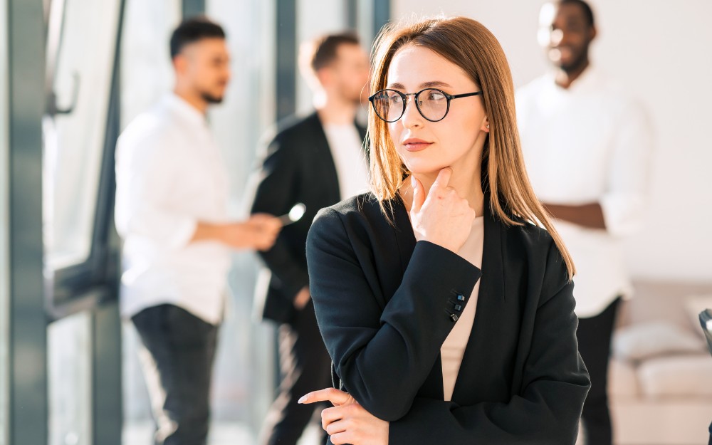 Pensive woman in the office, thinking about workers compensation for sexual harassment, three male coworers behind her
